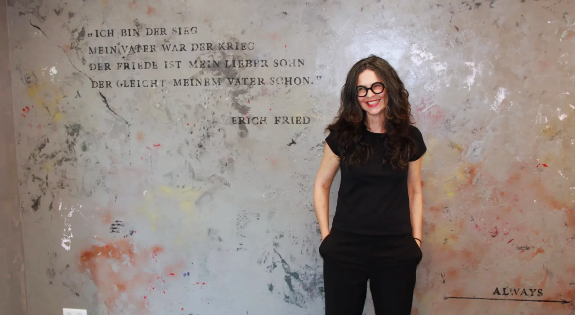 Sandra Landes vor einer von ihr gestalteten Wand mit einem Zitat von Erich Fried